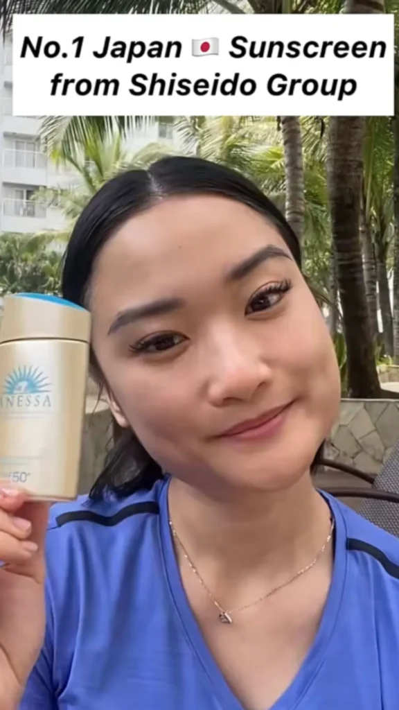 Influencer in a makeup-free selfie holding up the Anessa sunscreen bottle during a skincare routine video